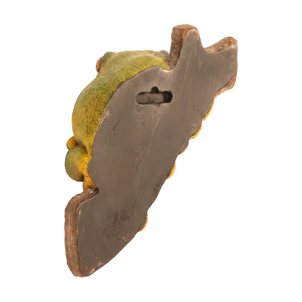 Decorative sculpture of a bright green and yellow tree frog with large orange eyes clinging to a textured brown branch.
