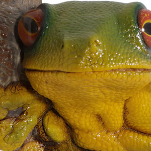 Decorative sculpture of a bright green and yellow tree frog with large orange eyes clinging to a textured brown branch.