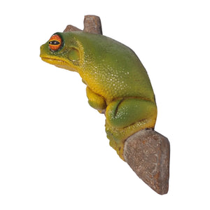 Decorative sculpture of a bright green and yellow tree frog with large orange eyes clinging to a textured brown branch.