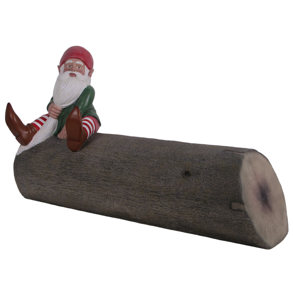 Decorative sculpture of a garden gnome wearing a red hat, green jacket, and striped leggings sitting on a horizontal textured brown log.