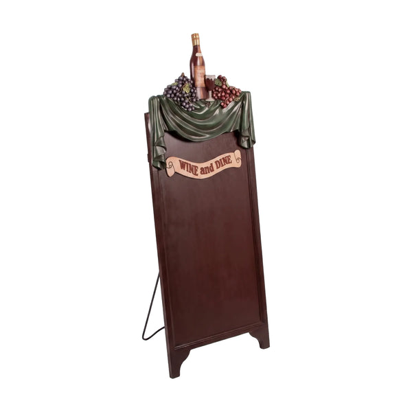 Decorative freestanding menu board featuring a dark writing surface topped with a sculpted wine bottle, grapes, and a Wine and Dine banner.