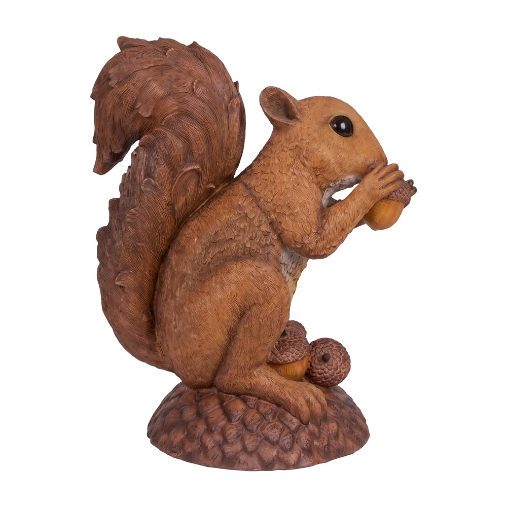 Decorative statue of a large brown squirrel holding an acorn, sitting upright on a textured base with additional acorns.