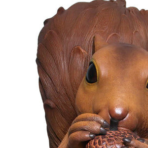 Decorative statue of a large brown squirrel holding an acorn, sitting upright on a textured base with additional acorns.