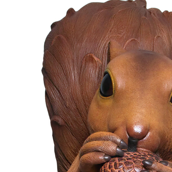 Decorative statue of a large brown squirrel holding an acorn, sitting upright on a textured base with additional acorns.