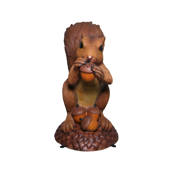 Decorative statue of a large brown squirrel holding an acorn, sitting upright on a textured base with additional acorns.