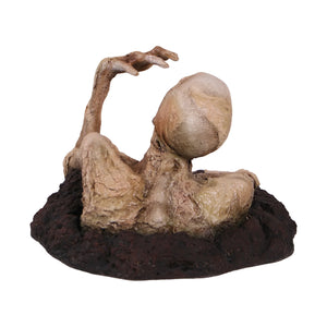 Decorative skeleton statue with mummified skin details and an open mouth, appearing to crawl out of a textured dirt base.