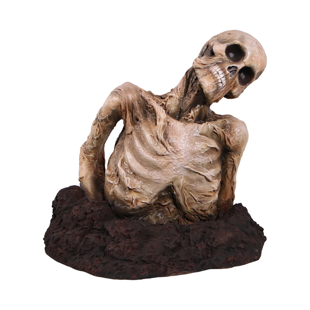Decorative skeleton statue featuring mummified skin details and a tilted skull, emerging from a textured dirt base.