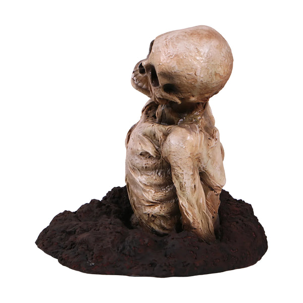 Decorative skeleton statue featuring mummified skin details and a tilted skull, emerging from a textured dirt base.