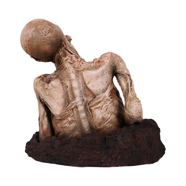 Decorative skeleton statue featuring mummified skin details and a tilted skull, emerging from a textured dirt base.